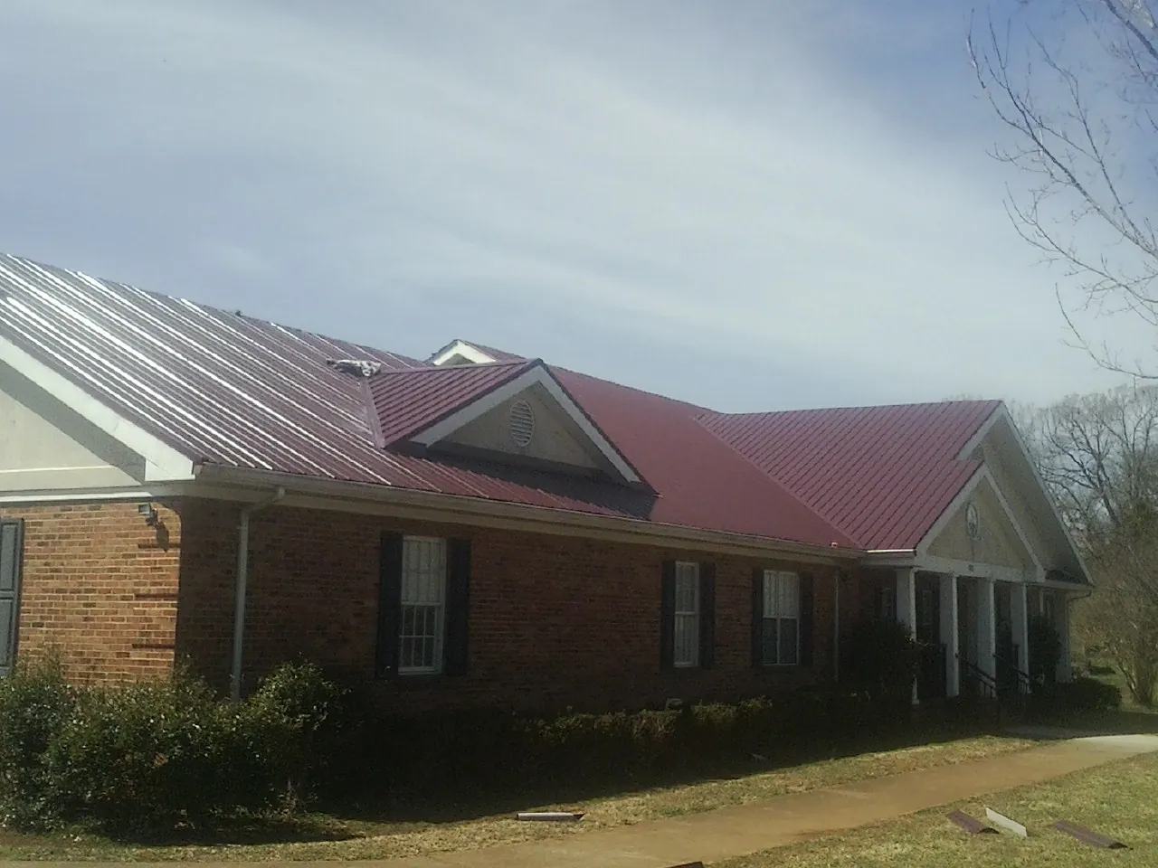 Red metal roof with gabled entries on a long brick building, from a Hail Damage Roof Repair job in Rancho Palos Verdes